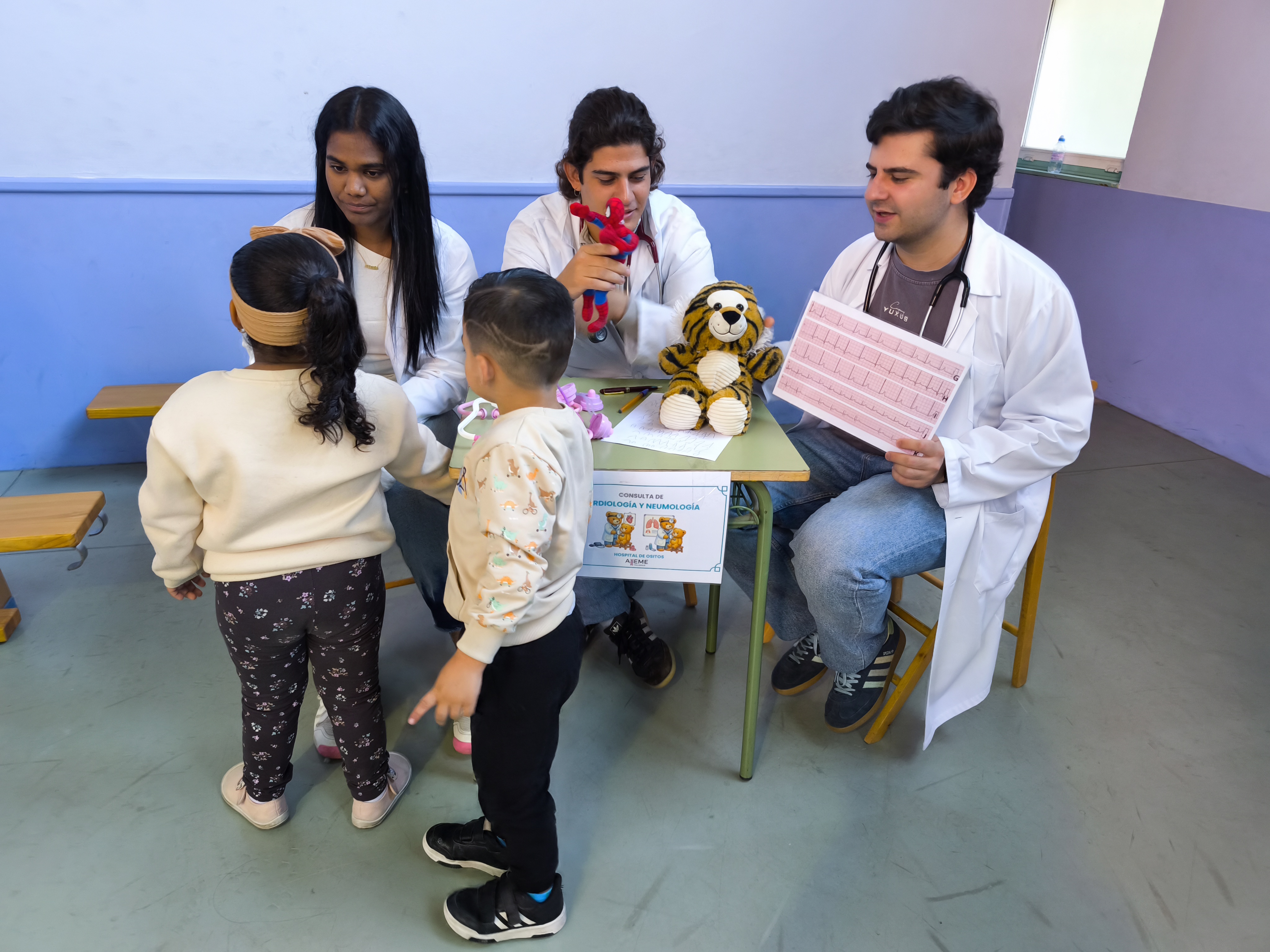 Estudiantes muestran a los niños un electrocardiograma y exploran a sus peluches en una consulta simulada