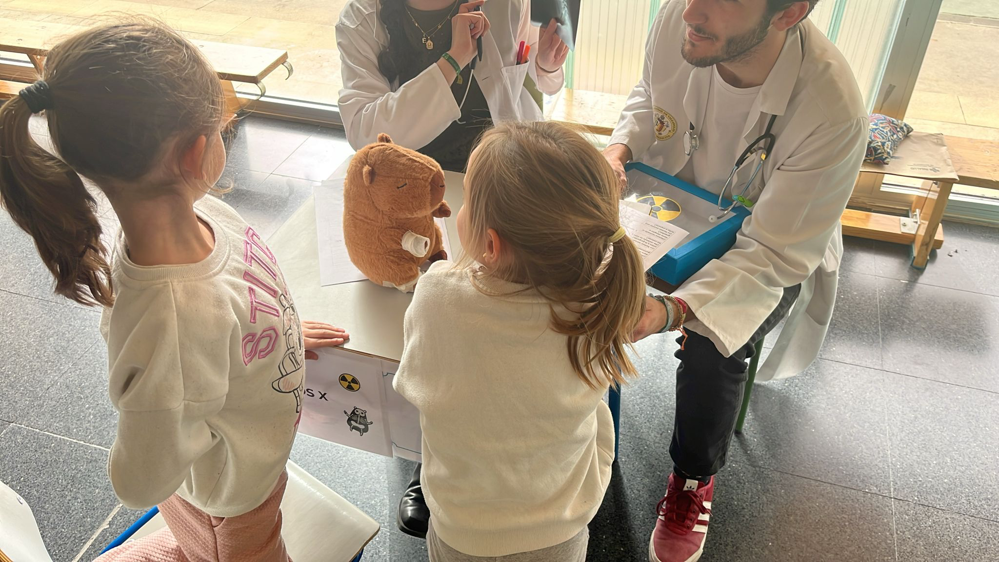 Dos niñas de espaldas acompañan a sus peluches en una consulta simulada de radiología con estudiantes de AIEME Valladolid