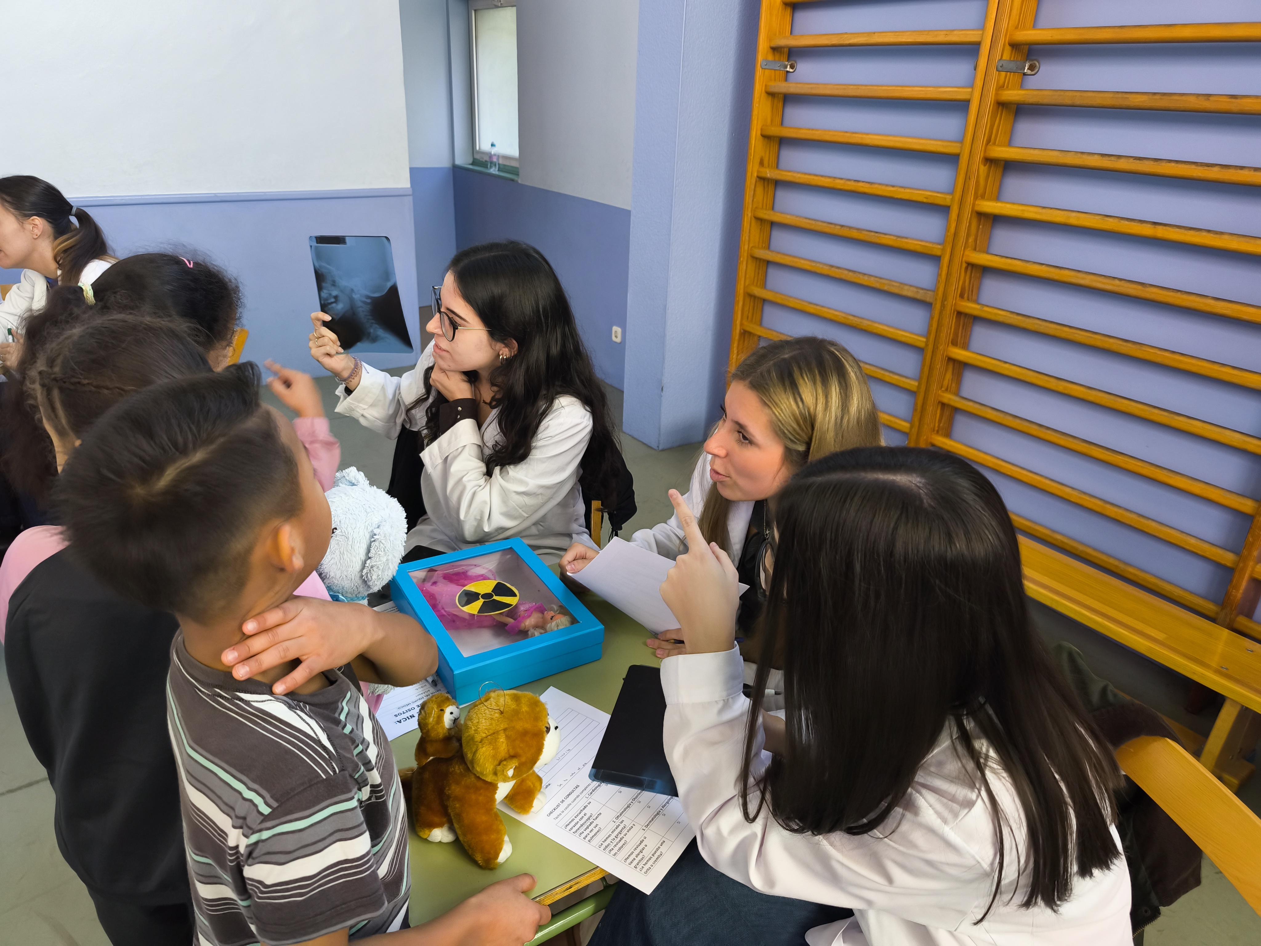 Estudiantes muestran una radiografía a los niños junto a sus peluches en una consulta simulada