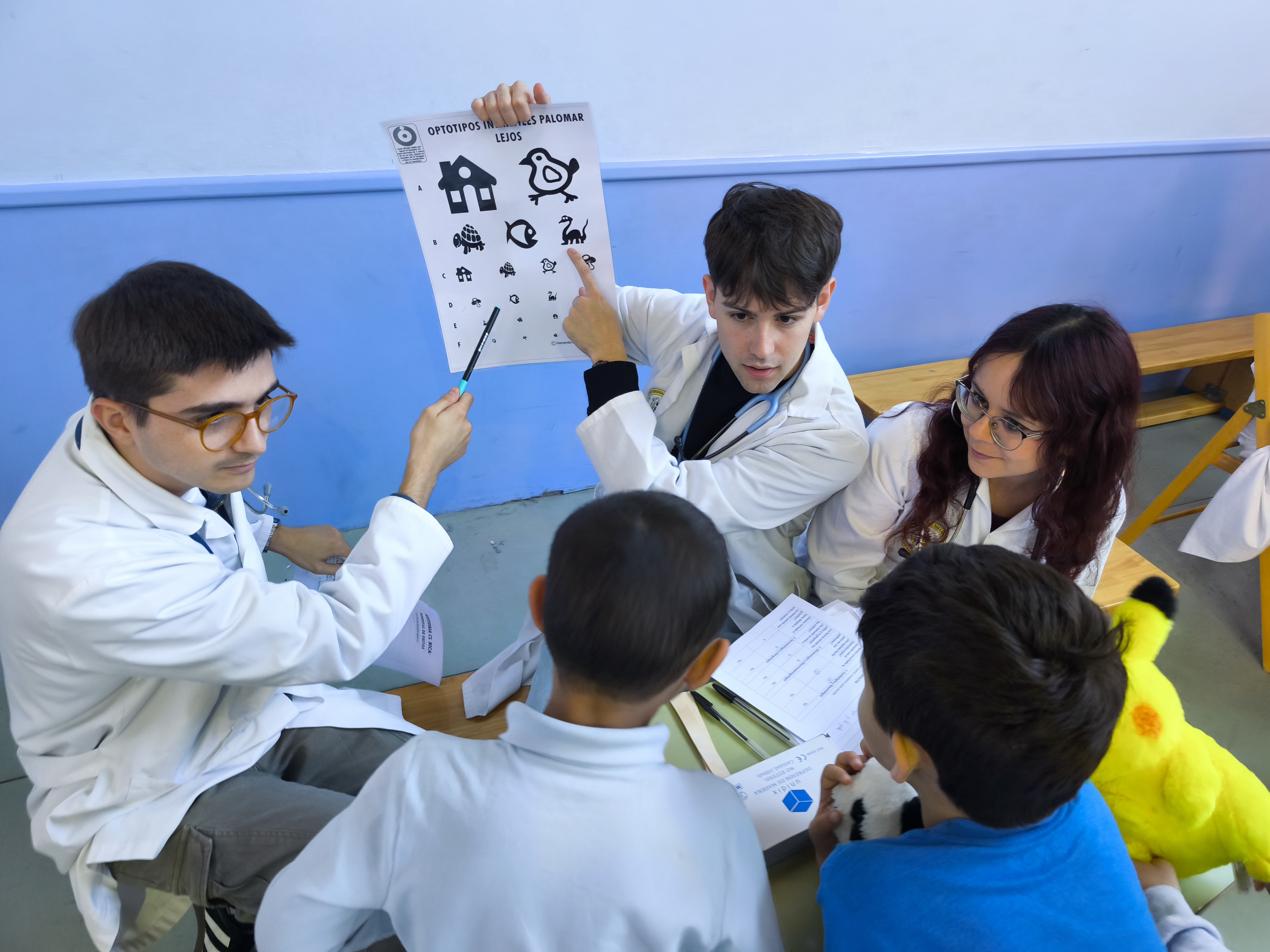 Estudiantes enseñan a los niños una lámina de dibujos para una revisión de la vista simulada